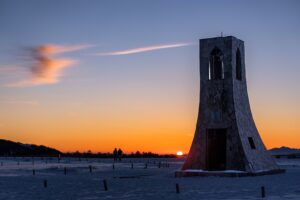 A solitary stone tower silhouetted against a glowing orange dawn sky over a snowy plain in central Japan, fine art landscape by Mitsuki