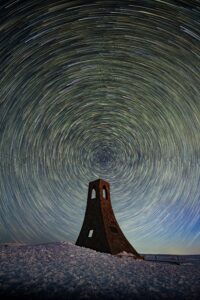 Circumpolar star trails circling above a solitary stone tower at night in central Japan, fine art photograph by Mitsuki