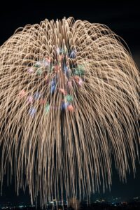 Golden chrysanthemum fireworks bursting over a city skyline in Japan, fine art photograph by Mitsuki
