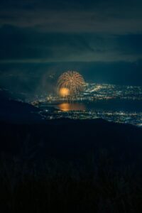 Fireworks reflected over a lakeside city at night, viewed from a mountain in central Japan, fine art photograph by Mitsuki